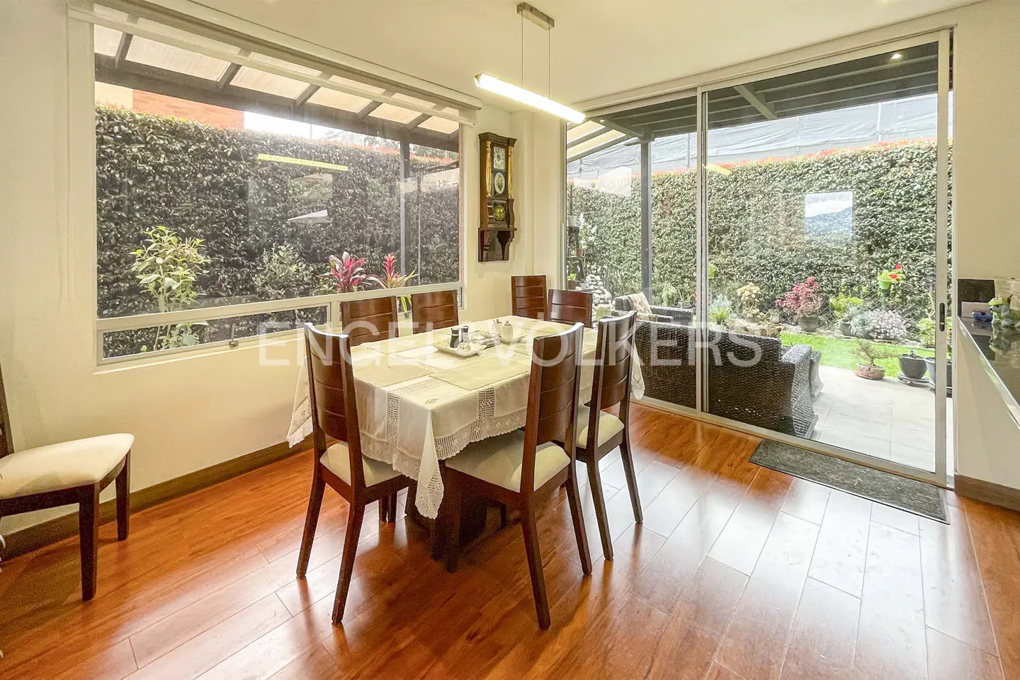 Dining room with wood floors, table with six chairs, and a view of a green garden through a large sliding glass door.