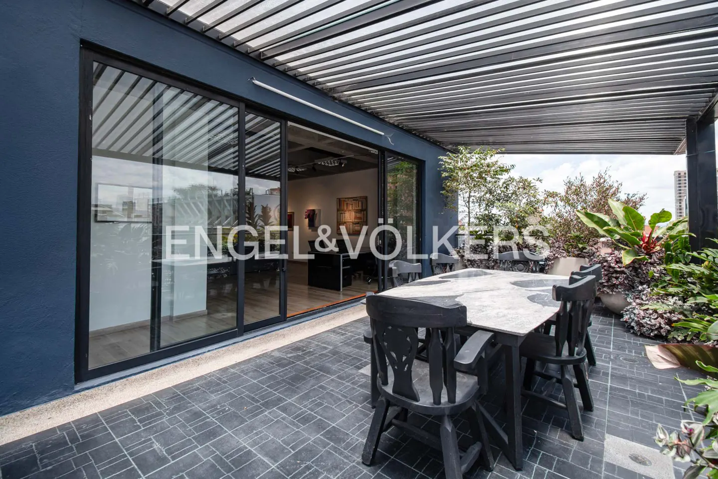 Outdoor patio with black table and chairs, plants, and a view of the city. Sliding glass doors lead to an interior space.