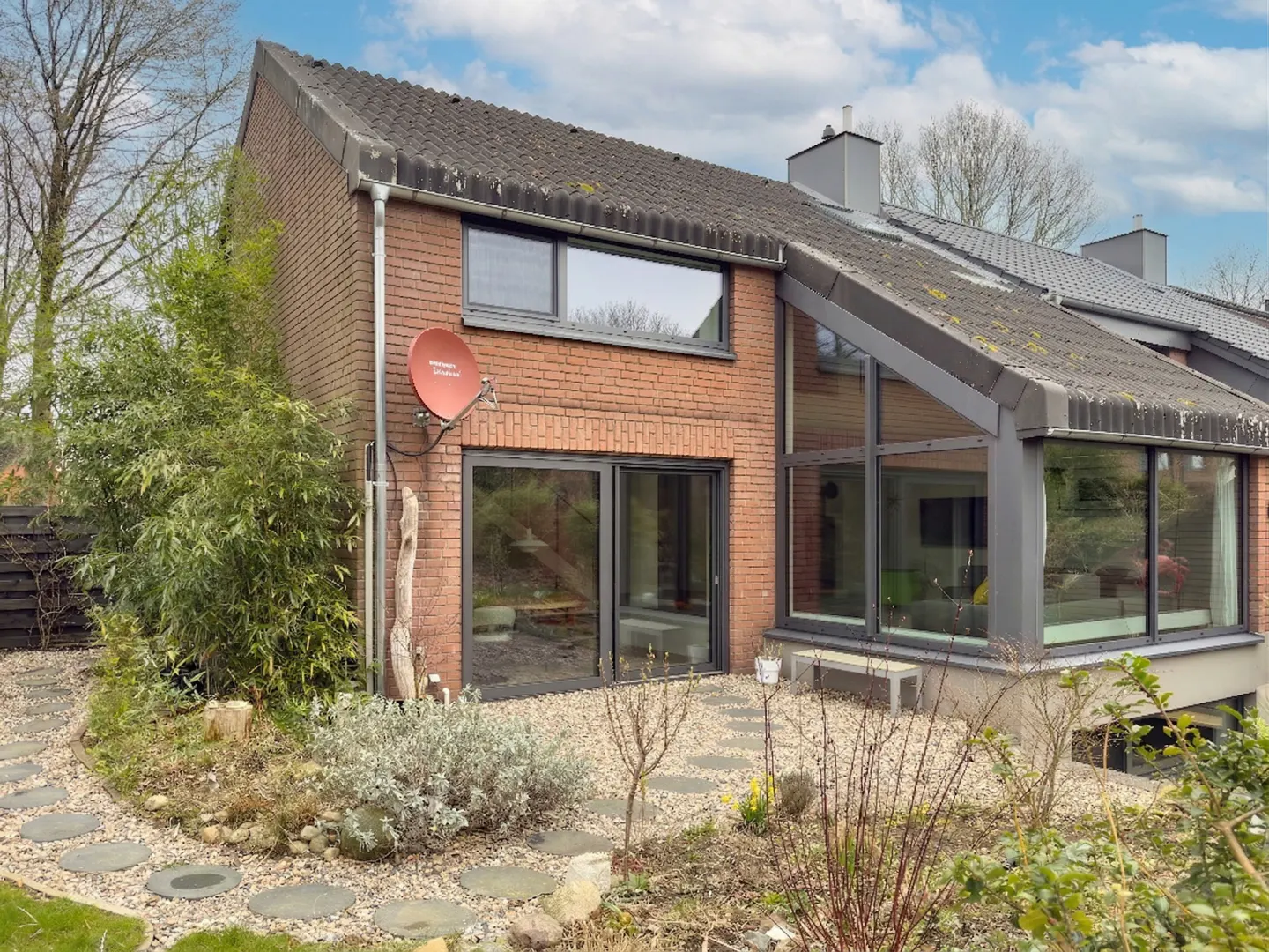 Back exterior of a brick house with a gray roof, large windows, and a satellite dish. A stone path leads to the house.
