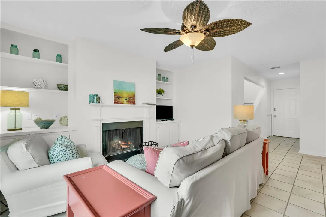 Bright living room with white sofas, fireplace, and built-in shelves. A brown ceiling fan hangs above.