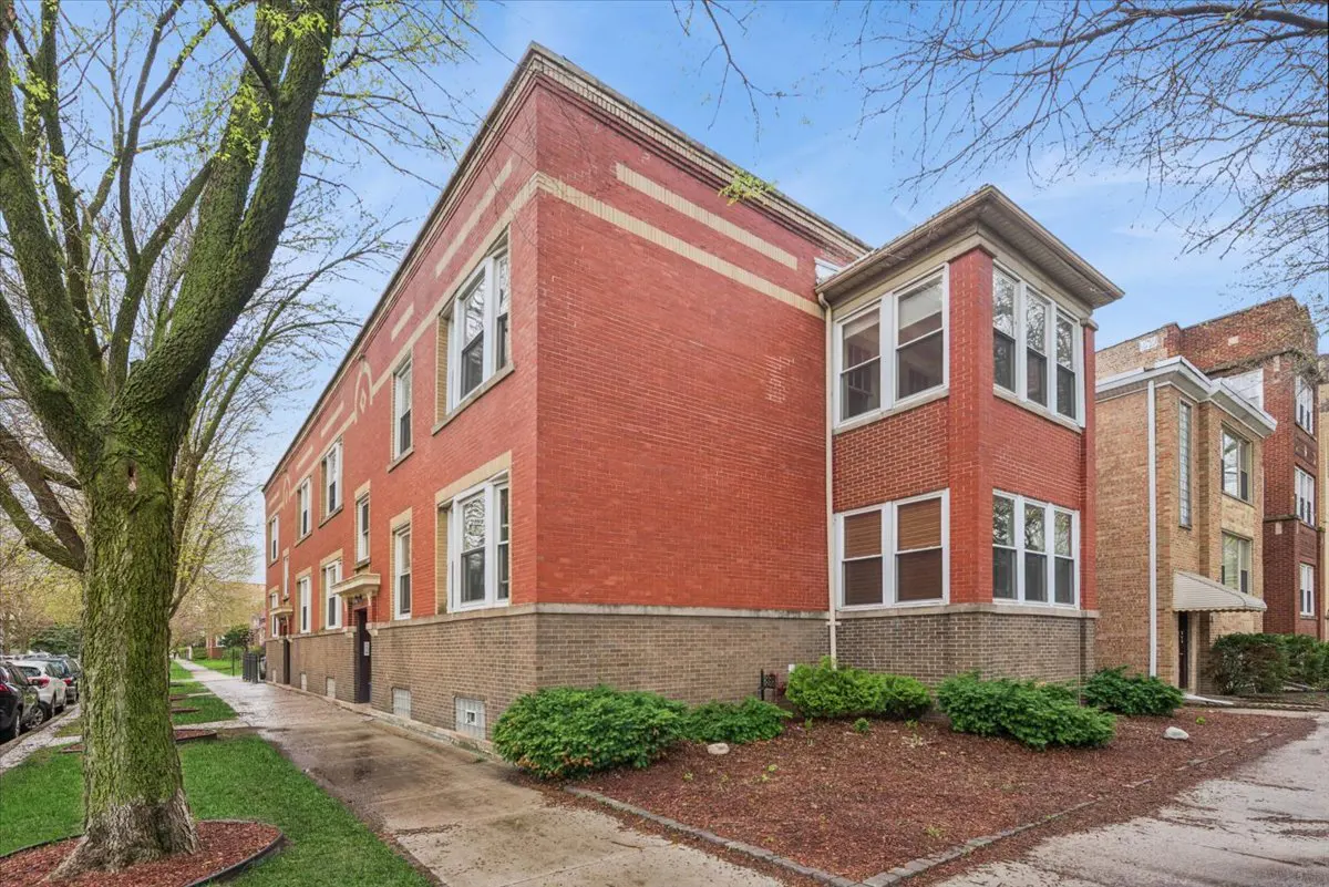 Exterior view of a three-story red brick apartment building with white-framed windows and a landscaped yard.