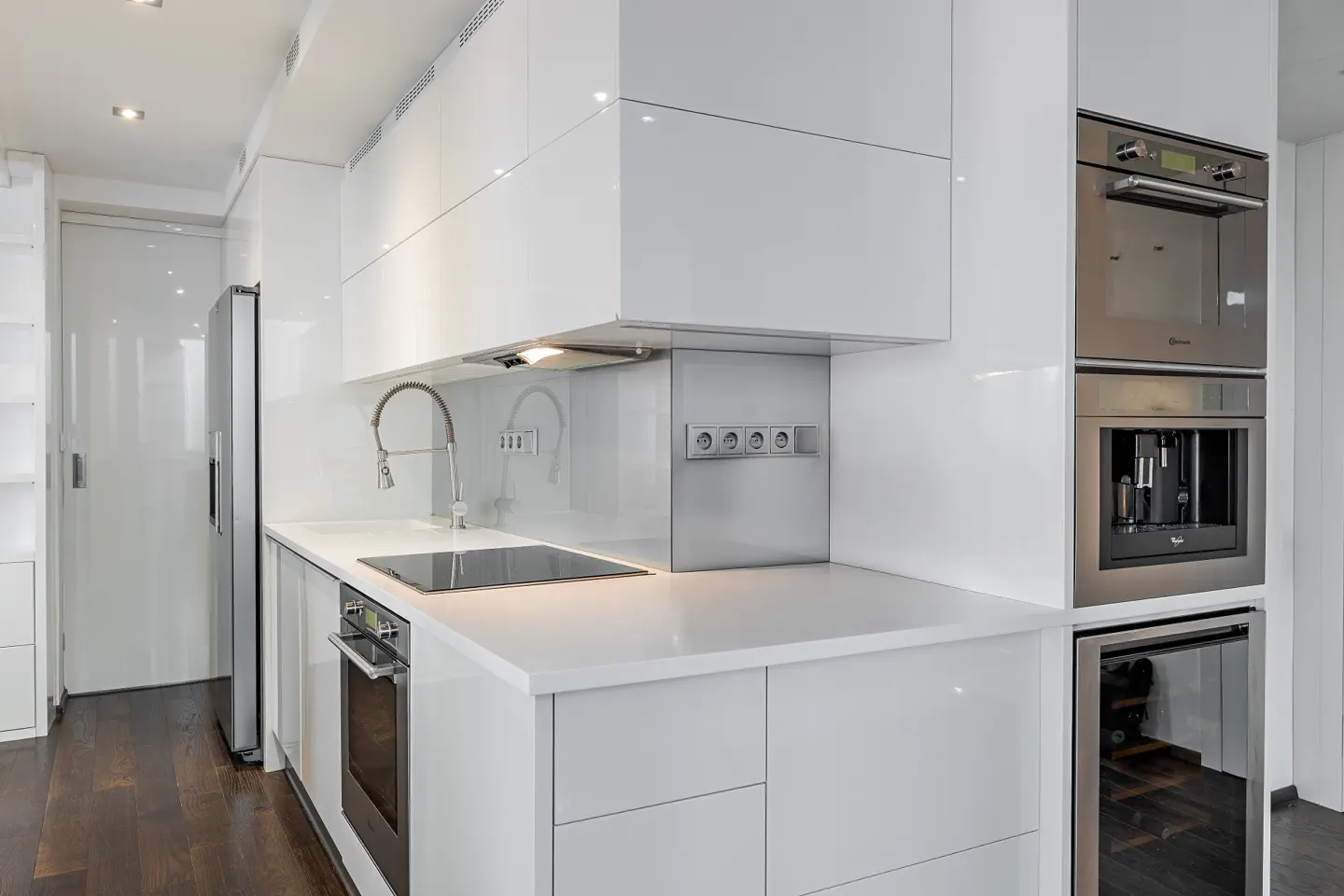 Modern kitchen with white cabinets, stainless steel appliances, and dark wood floors.