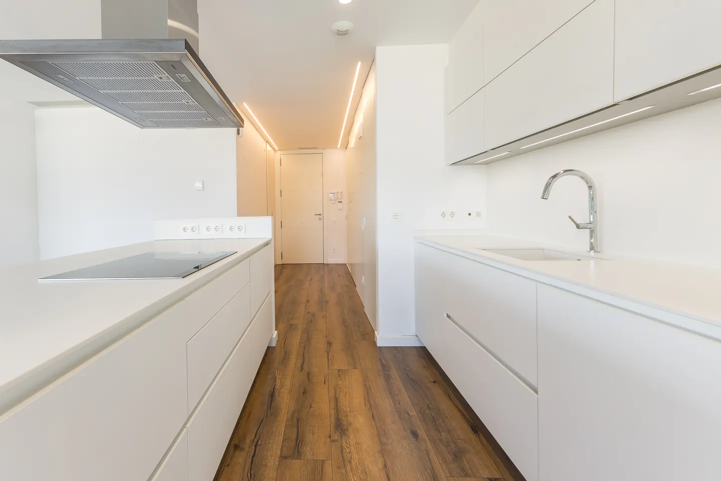 Bright, modern kitchen with white cabinets, countertops, and walls. Stainless steel range hood and faucet. Wood-look flooring.