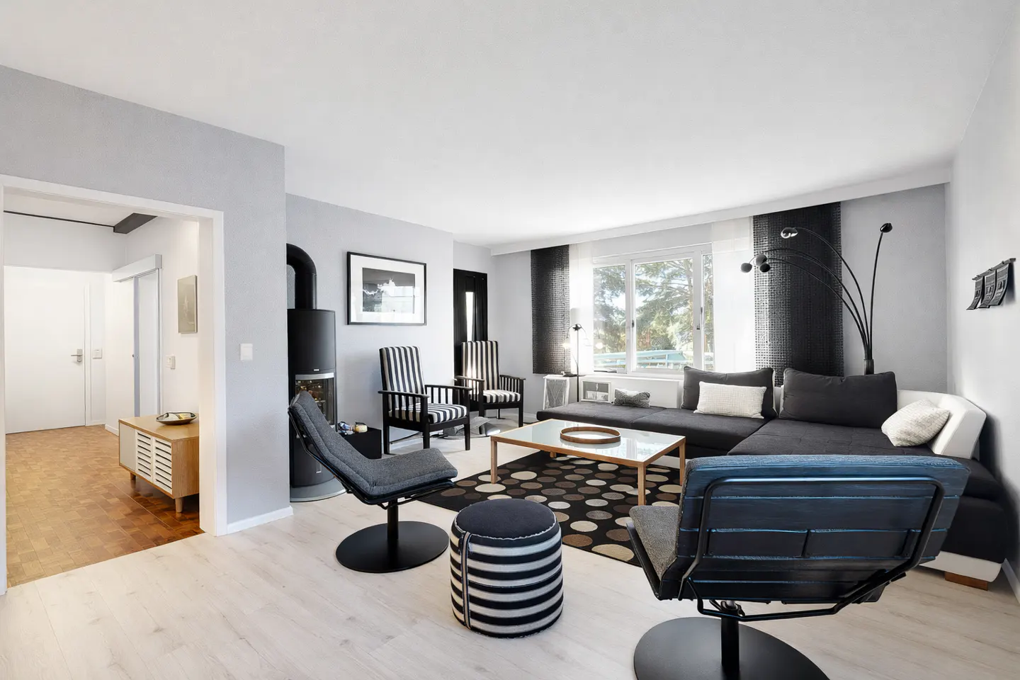 Bright living room with gray walls, wood floors, and black and white furniture. A black fireplace stands near striped chairs.