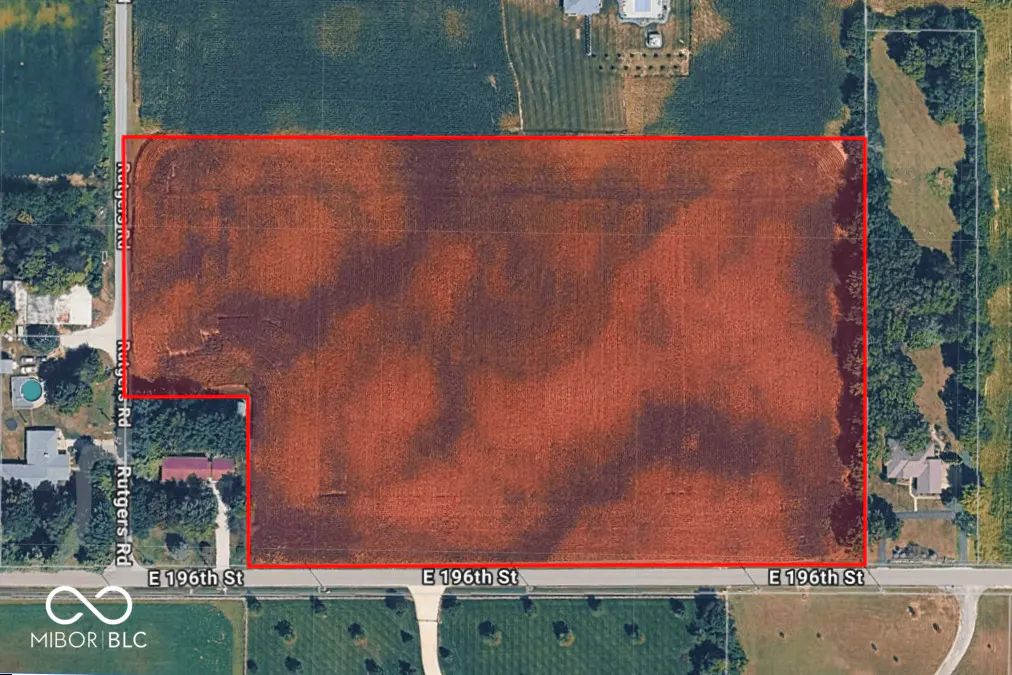 Aerial view of a large, rectangular, reddish-brown field outlined in red, bordered by roads and greenery.