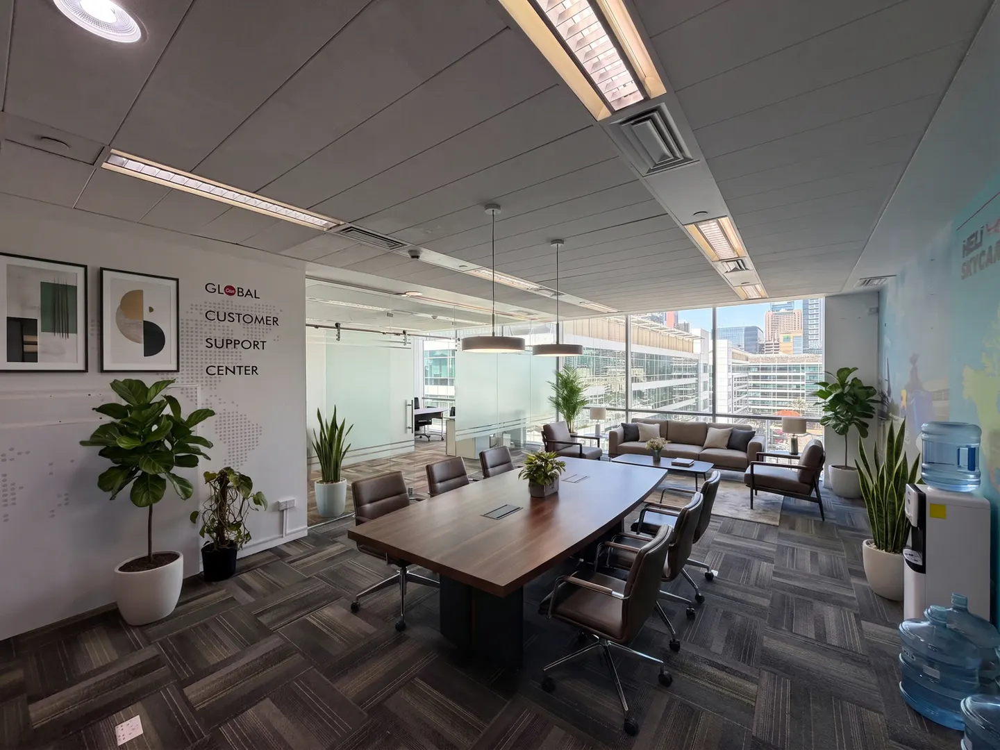 Modern office conference room with a large wooden table, leather chairs, potted plants, and city views through windows.