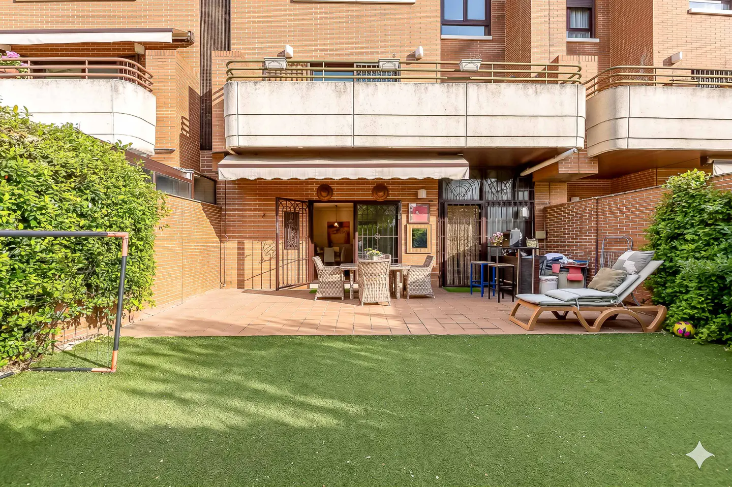 A backyard with a brick building, a patio with furniture, a lawn, and a soccer goal.