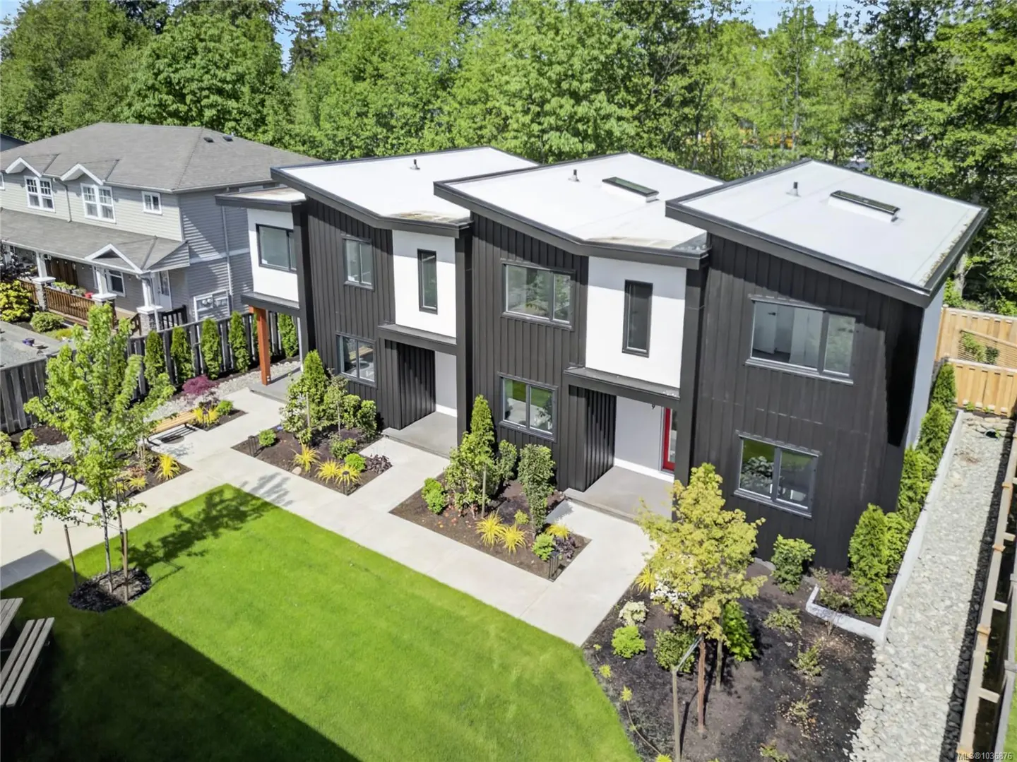 Aerial view of modern black and white townhouses with flat roofs, surrounded by green lawns and trees.