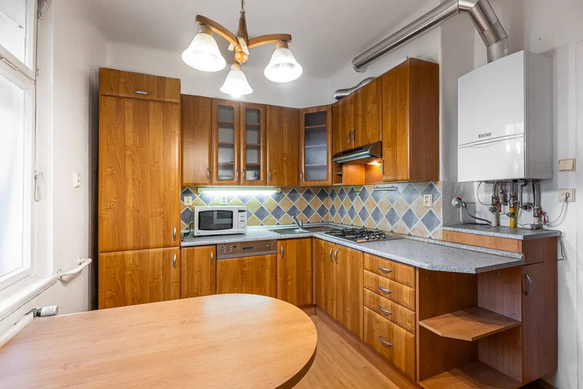 Kitchen with wooden cabinets, grey countertops, diamond-patterned backsplash, and a wall-mounted boiler unit.