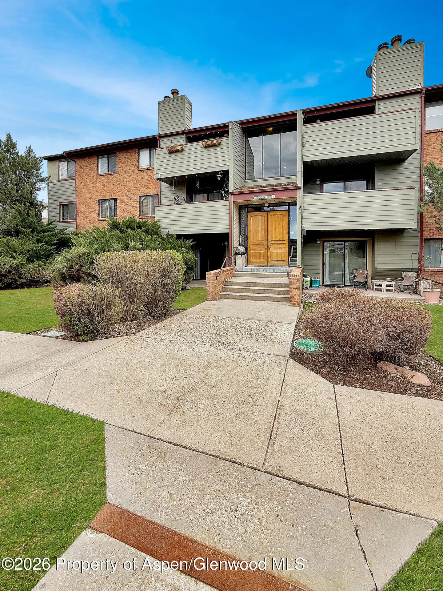 Exterior view of a multi-story apartment building with brick and green siding, a concrete walkway, and green grass.
