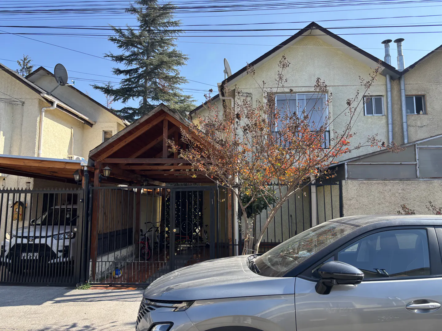 A two-story beige house with a brown roof and a silver car parked in front.