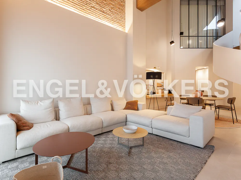 Modern living room with a large white sectional sofa, two coffee tables, and a patterned rug under a high brick wall.