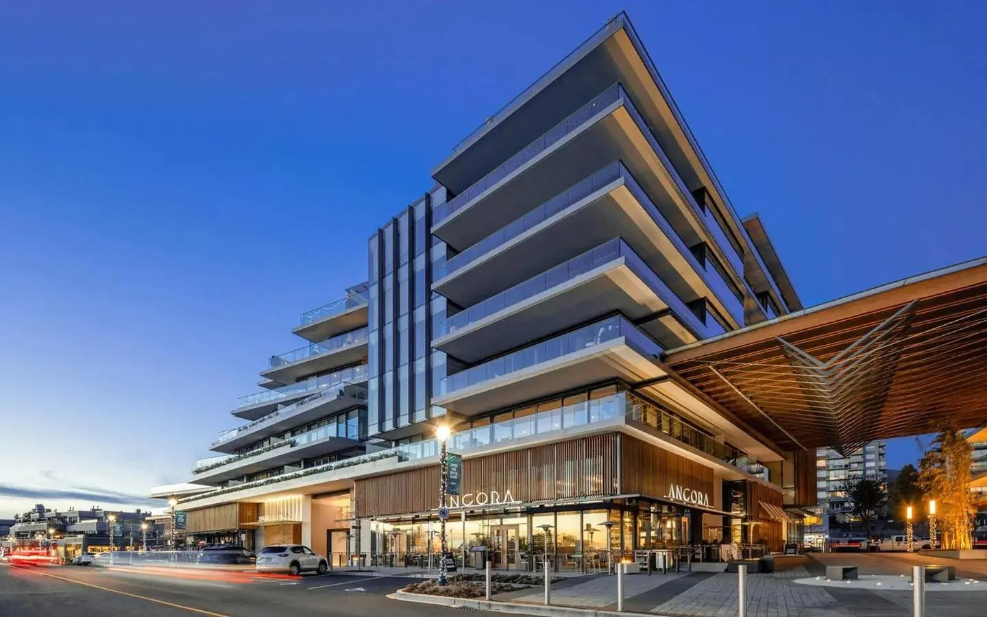 Modern condo building with glass balconies and a restaurant called Ancora on the ground floor at dusk.