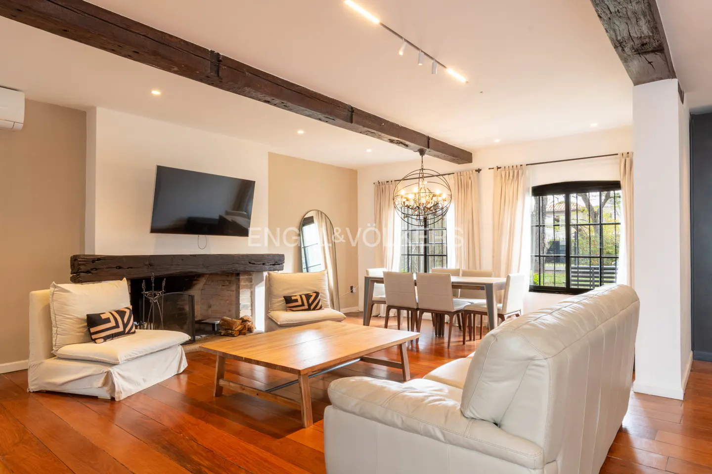 Living room with white sofas, wooden coffee table, fireplace, and dining area with a chandelier and hardwood floors.