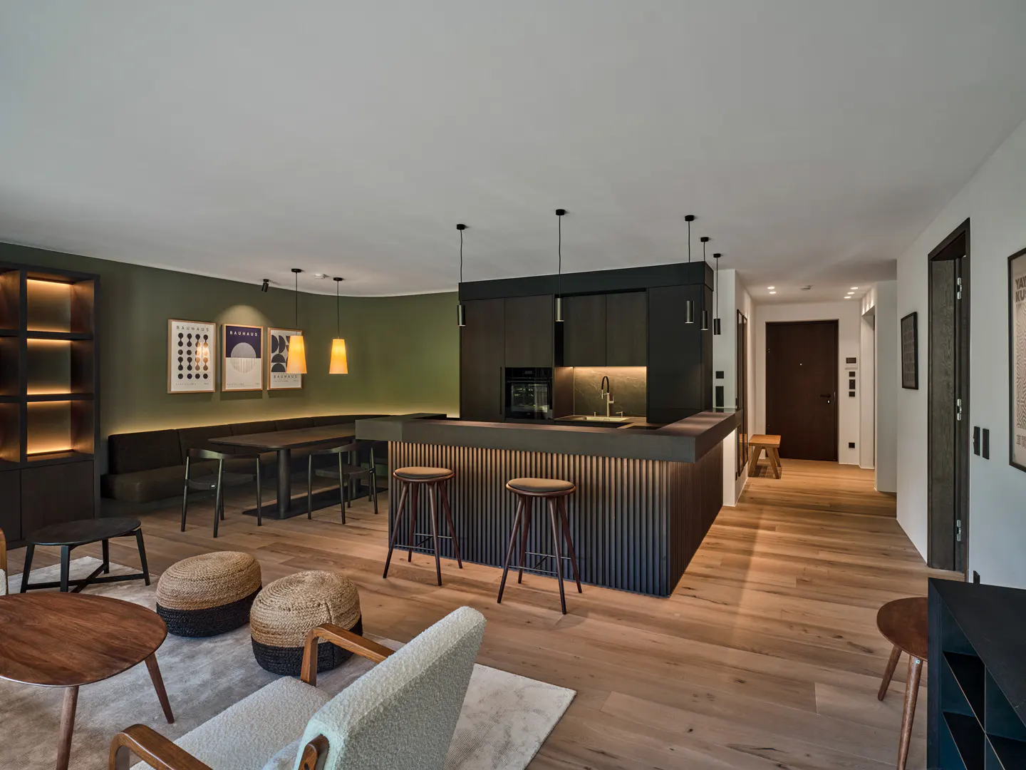 Modern open-plan kitchen with a black slatted island, bar stools, dining area, and olive green walls on light wood floors.