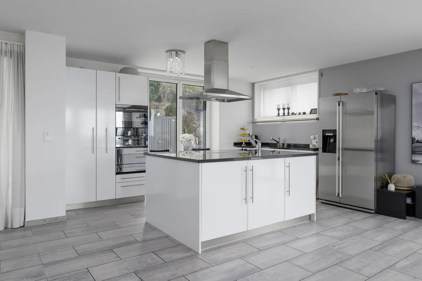 Bright kitchen with white cabinets, stainless steel appliances, and a black countertop island. Gray tile floor and modern lighting.