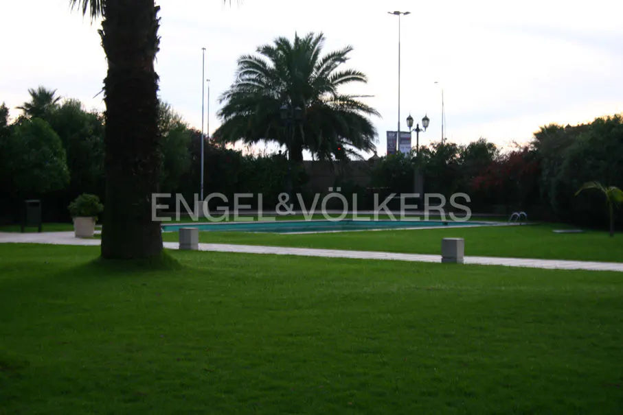 Lush green lawn with a pool in the background, framed by palm trees and greenery. The Engel & Völkers logo is superimposed on the image.