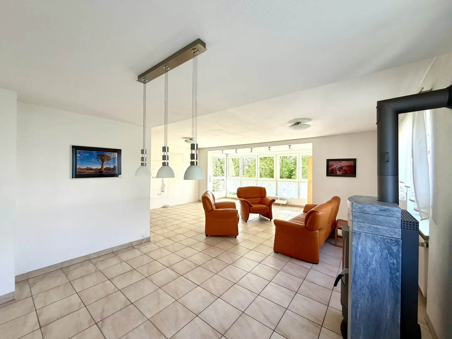 Bright living room with tan tile floors, white walls, and orange leather furniture. A modern fireplace sits near a window.
