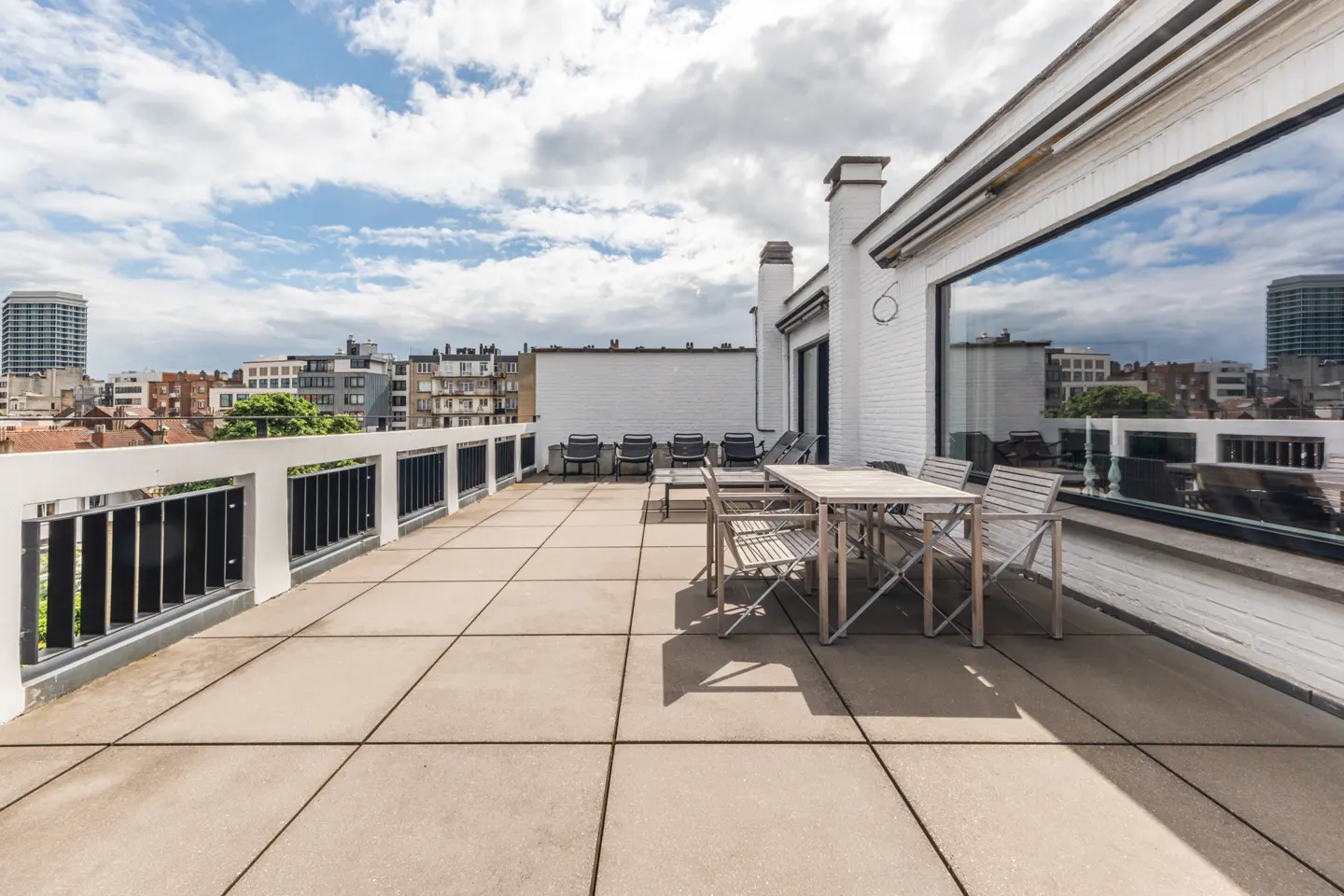 Spacious rooftop terrace with tiled flooring, outdoor dining set, and a panoramic view of the city skyline under a blue sky.