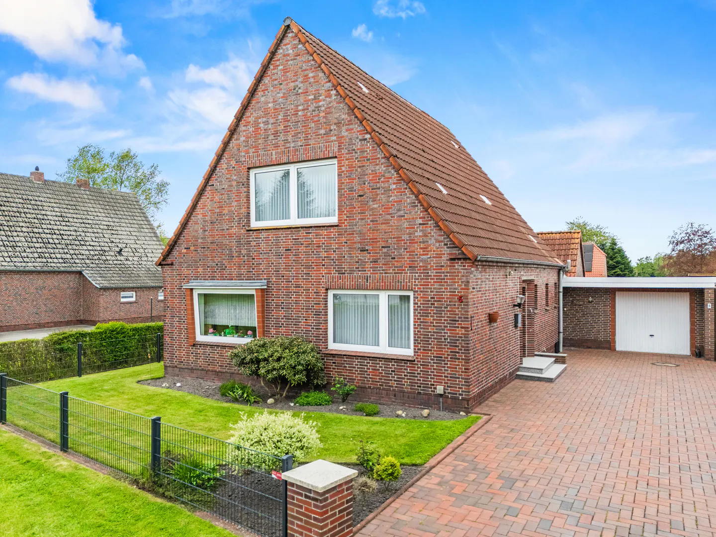 A two-story brick house with a red tile roof, white windows, and a brick driveway on a sunny day.