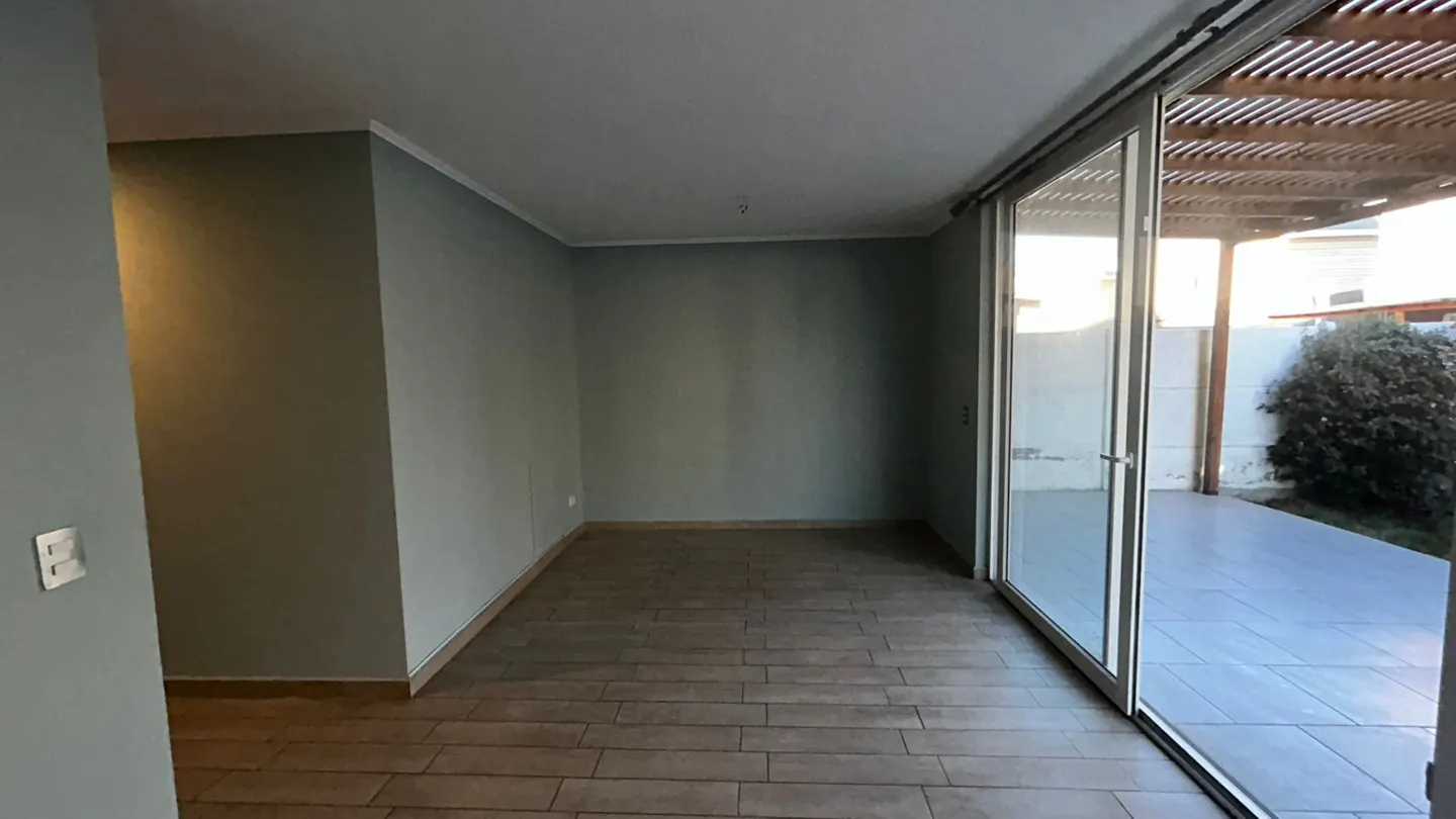 Empty room with gray walls and wood-look tile floor. Sliding glass doors open to a patio and garden.
