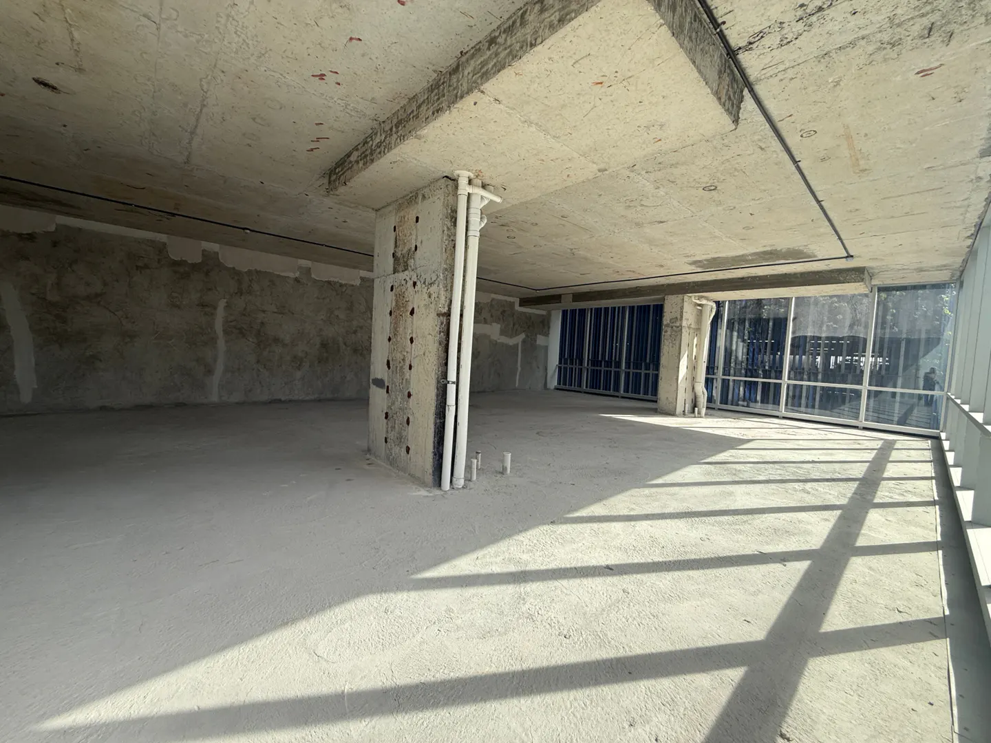 Unfinished commercial space with concrete floors, walls, and ceiling. Sunlight streams through large windows.