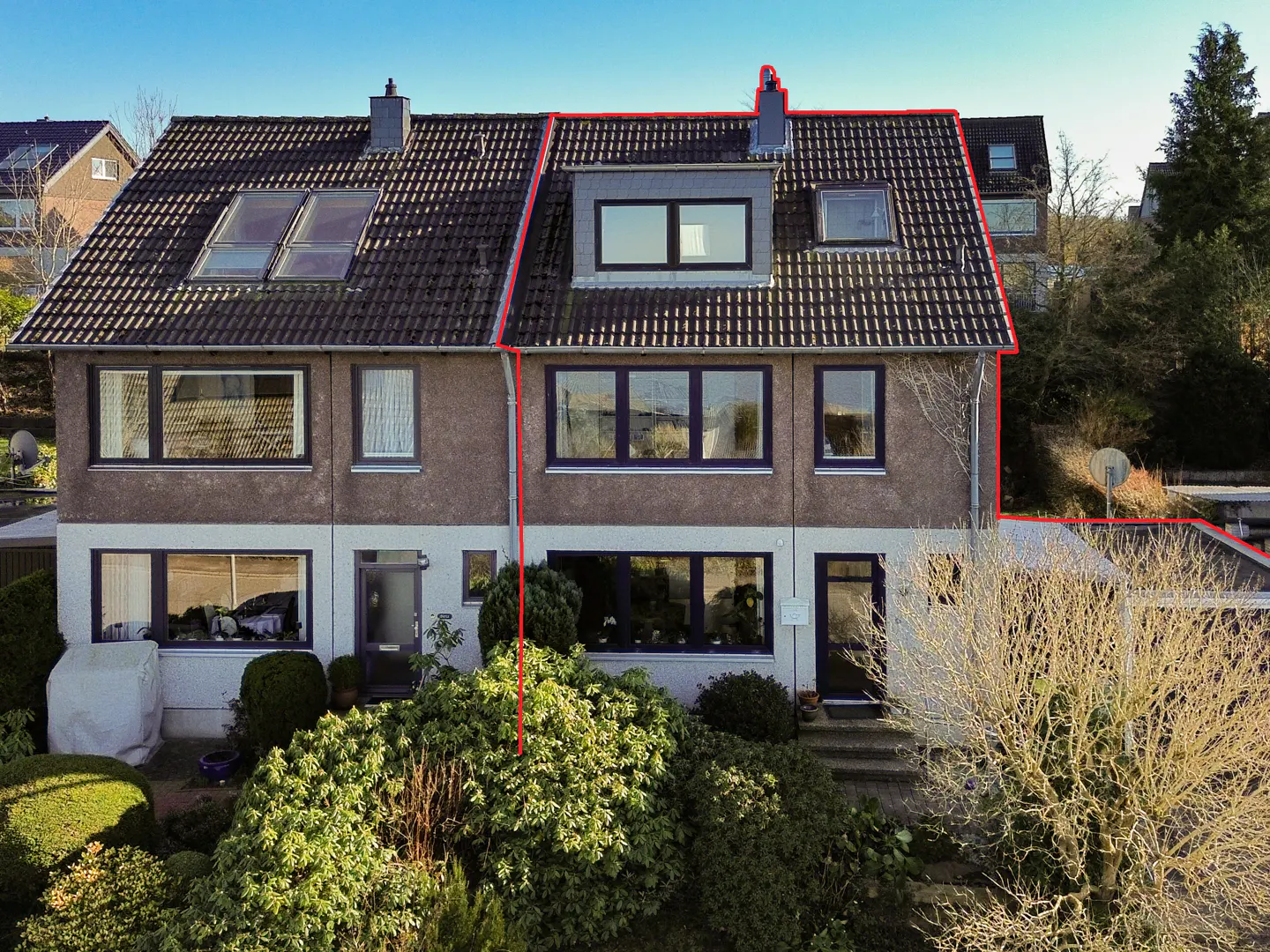 Exterior view of a two-story semi-detached house with a tiled roof, dormer window, and lush front garden.