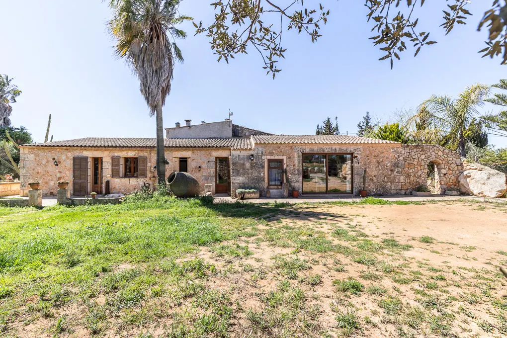 Exterior view of a one-story stone house with a tiled roof and a green lawn in front.