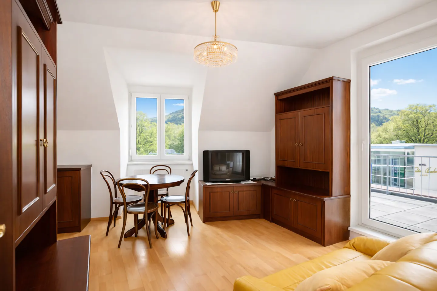 Bright living room with wood floors, a round table with four chairs, and a yellow sofa. A chandelier hangs from the white ceiling.