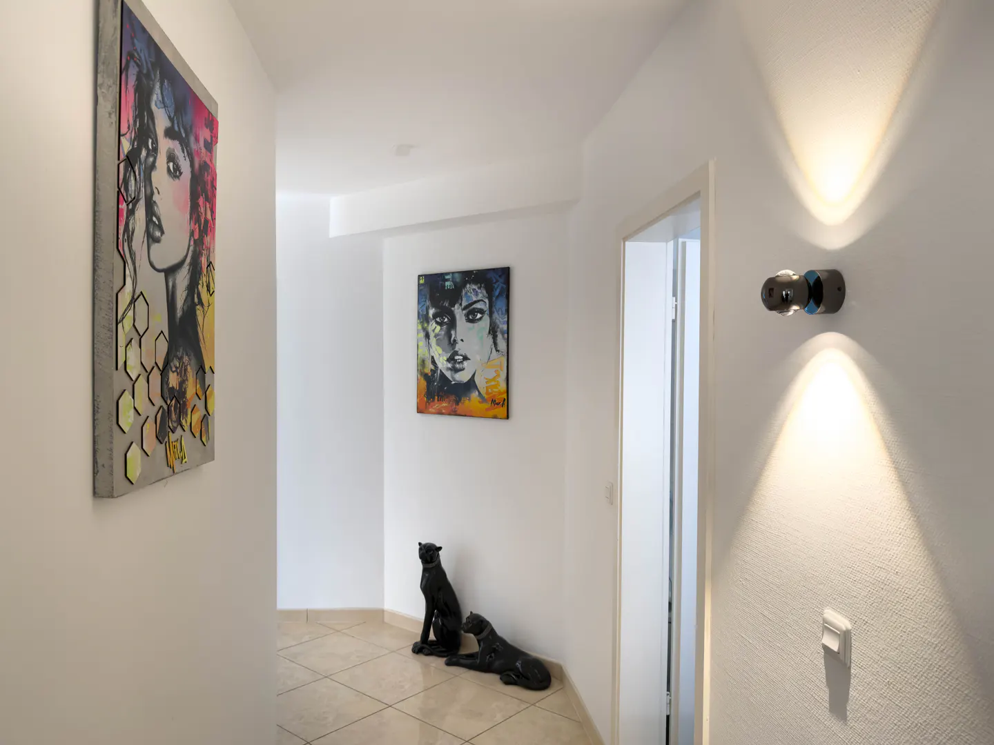 Hallway with art: a colorful portrait hangs on the left wall, and two black panther statues sit near another portrait at the end of the hall.