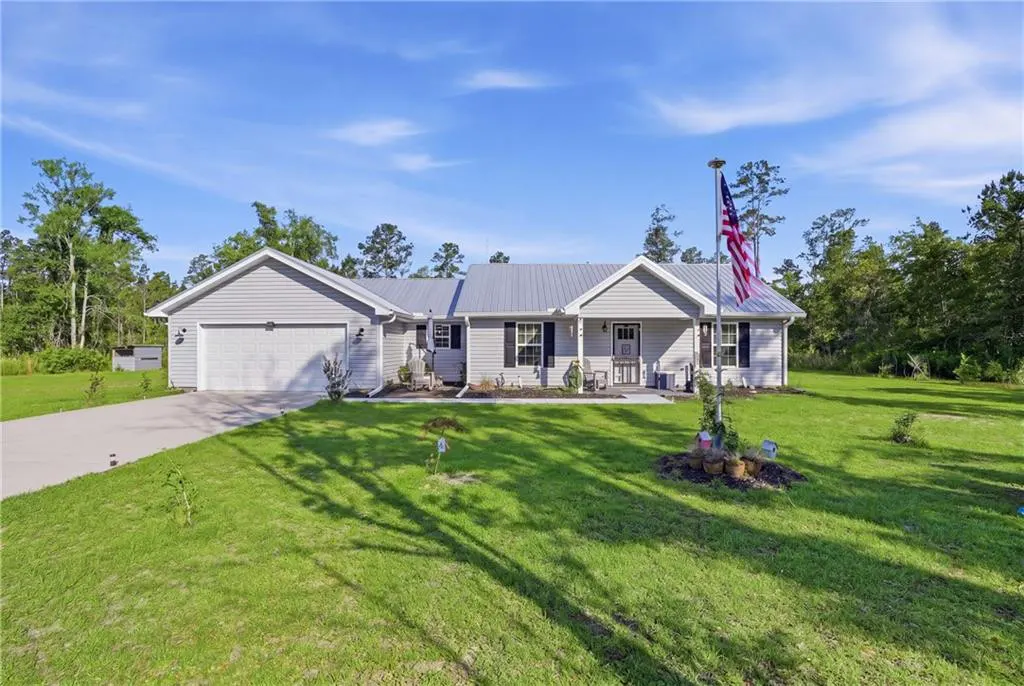 A single-story gray house with a metal roof, a garage, and an American flag in the yard.