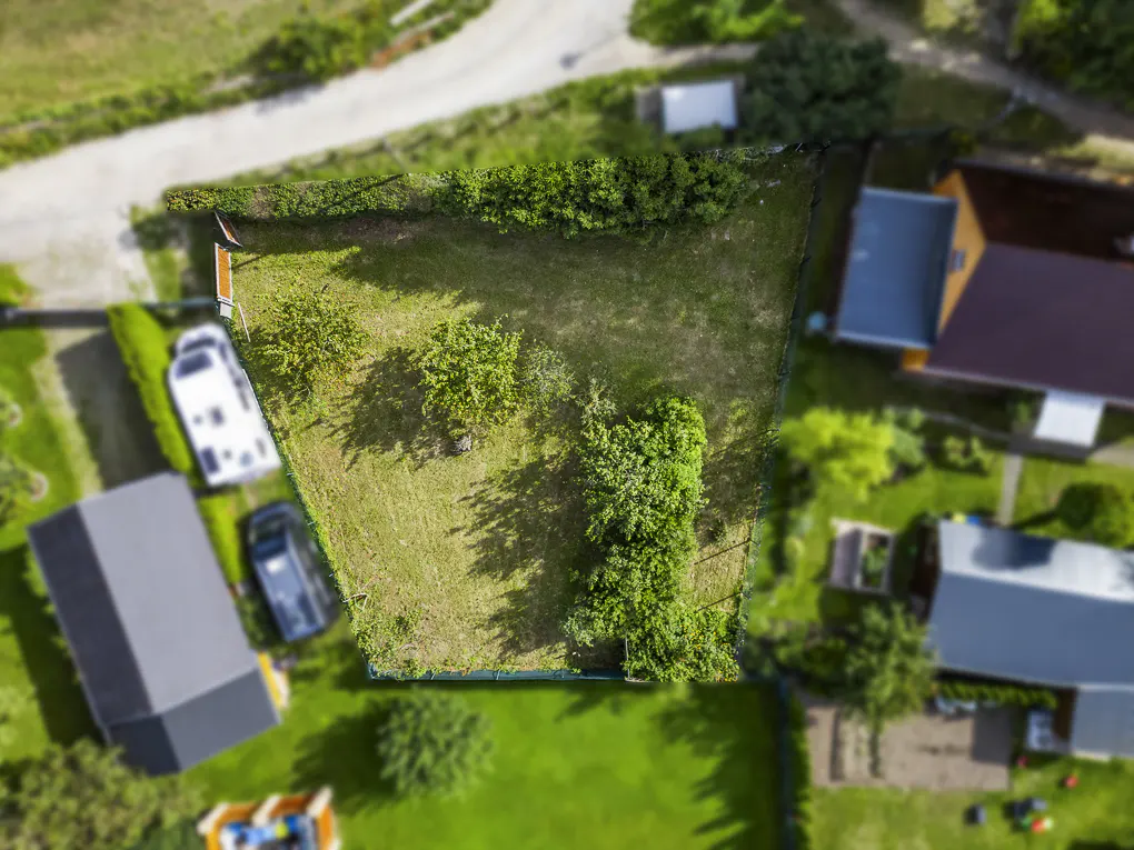 Aerial view of a grassy, fenced property with trees, a boat, and cars nearby.