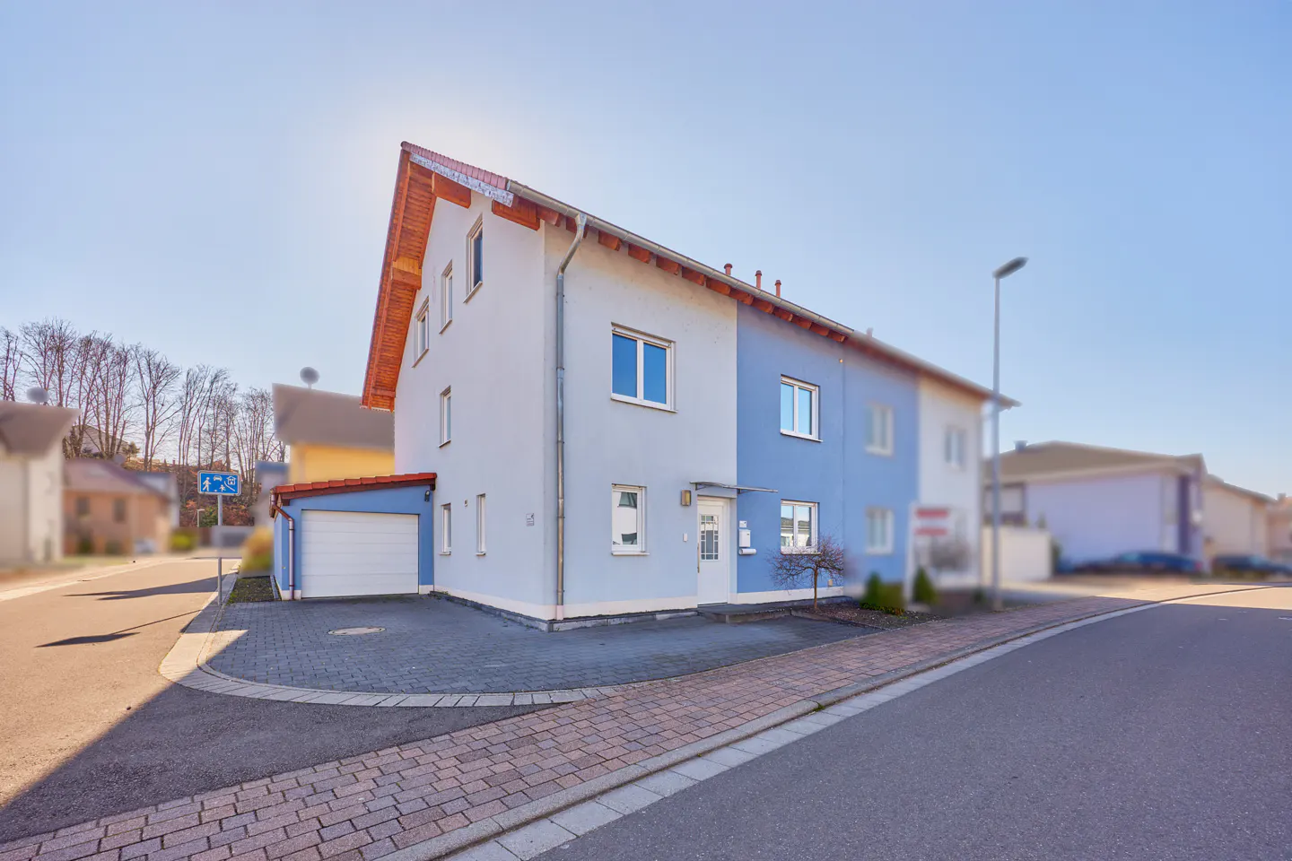 Two-story house with a white garage, light blue and blue walls, and a red roof on a sunny day.