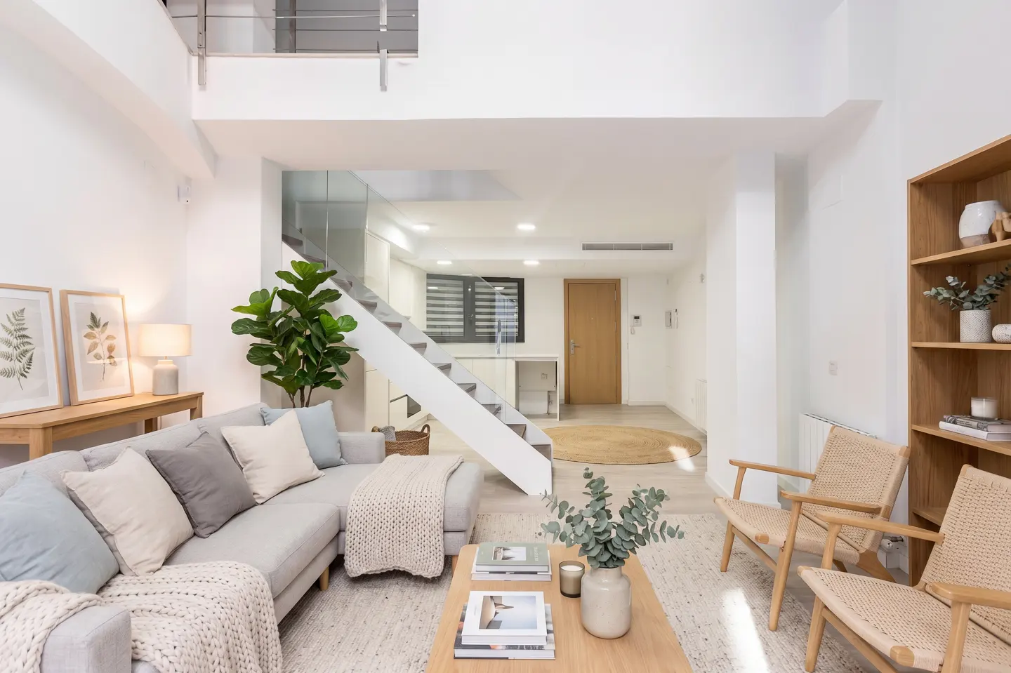 Bright, modern living room with a gray sofa, wooden coffee table, and white walls. A staircase leads to an upper level.
