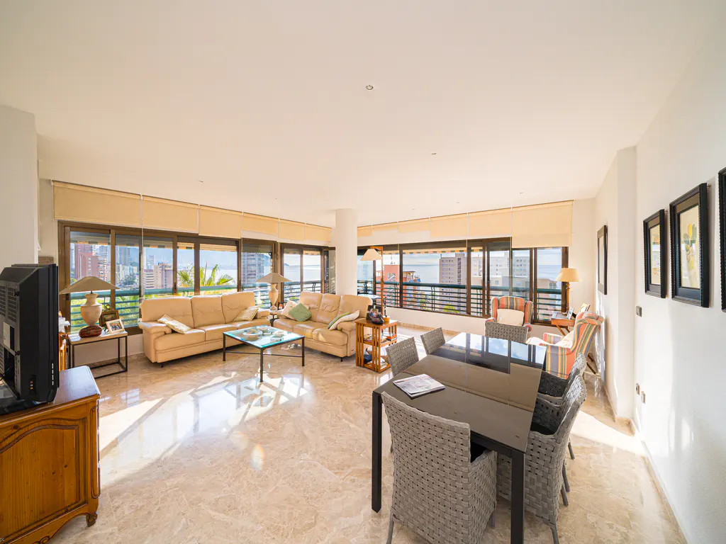 Bright, open living and dining area with beige sofas, a black dining table, and a city view through large windows.
