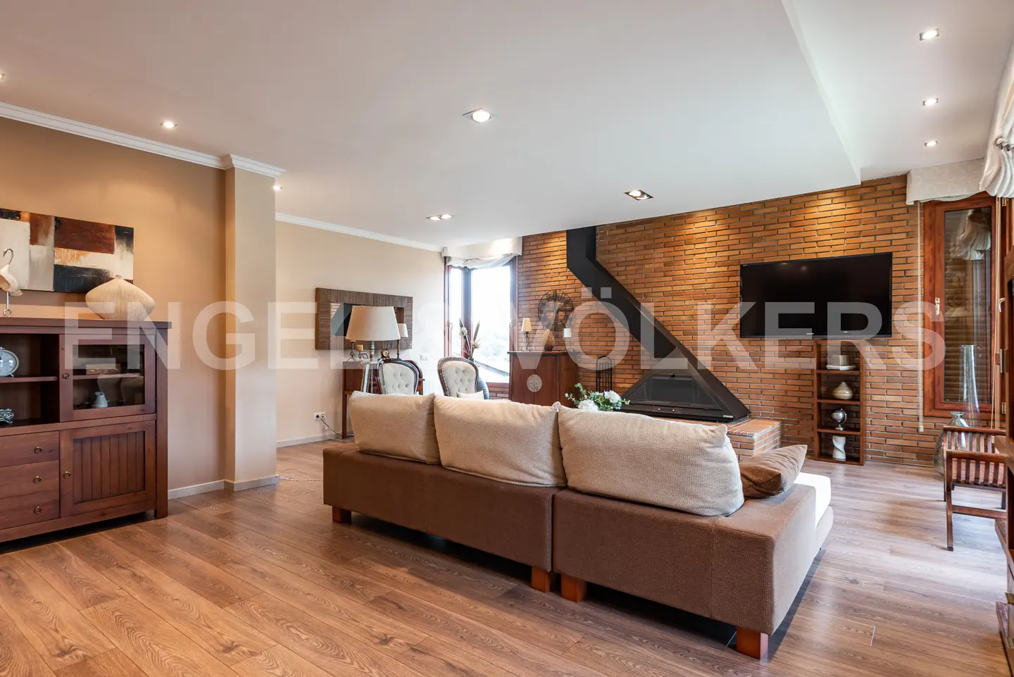 Living room with a brown sectional sofa, wood floors, brick accent wall, fireplace, and wall-mounted television.