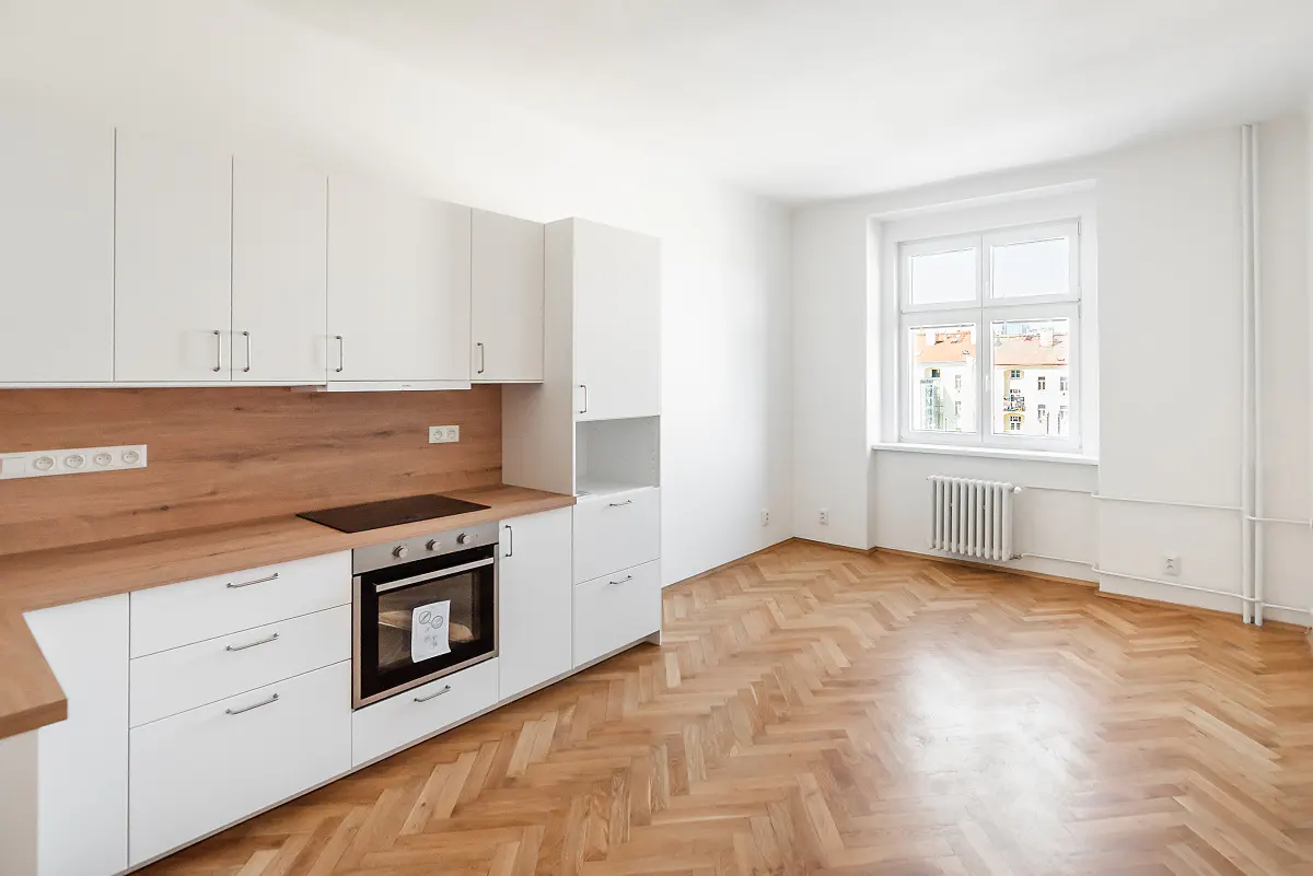 Bright, modern kitchen with white cabinets, wood countertops, and herringbone wood floors. A window overlooks a city view.