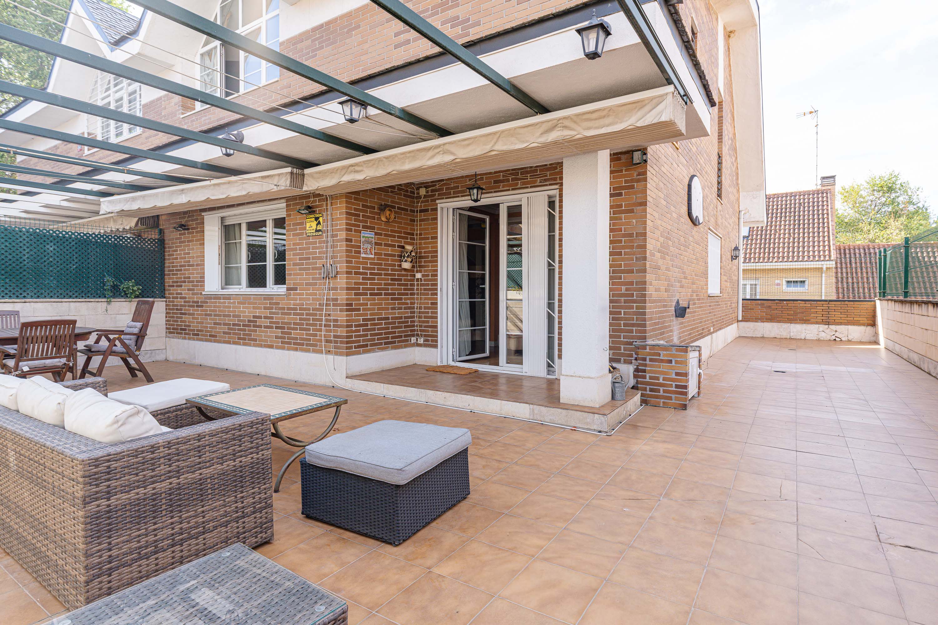 Spacious brick patio with wicker outdoor furniture, a pergola, and sliding glass doors leading into the house. [AI-generated text]