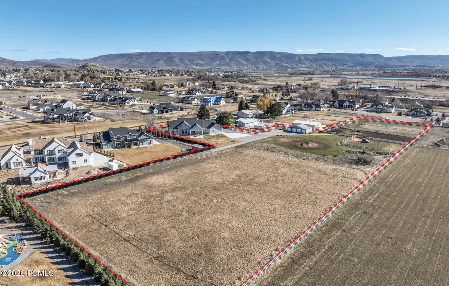 Aerial view of a large, vacant lot outlined in red, with houses, mountains, and a blue sky in the background.