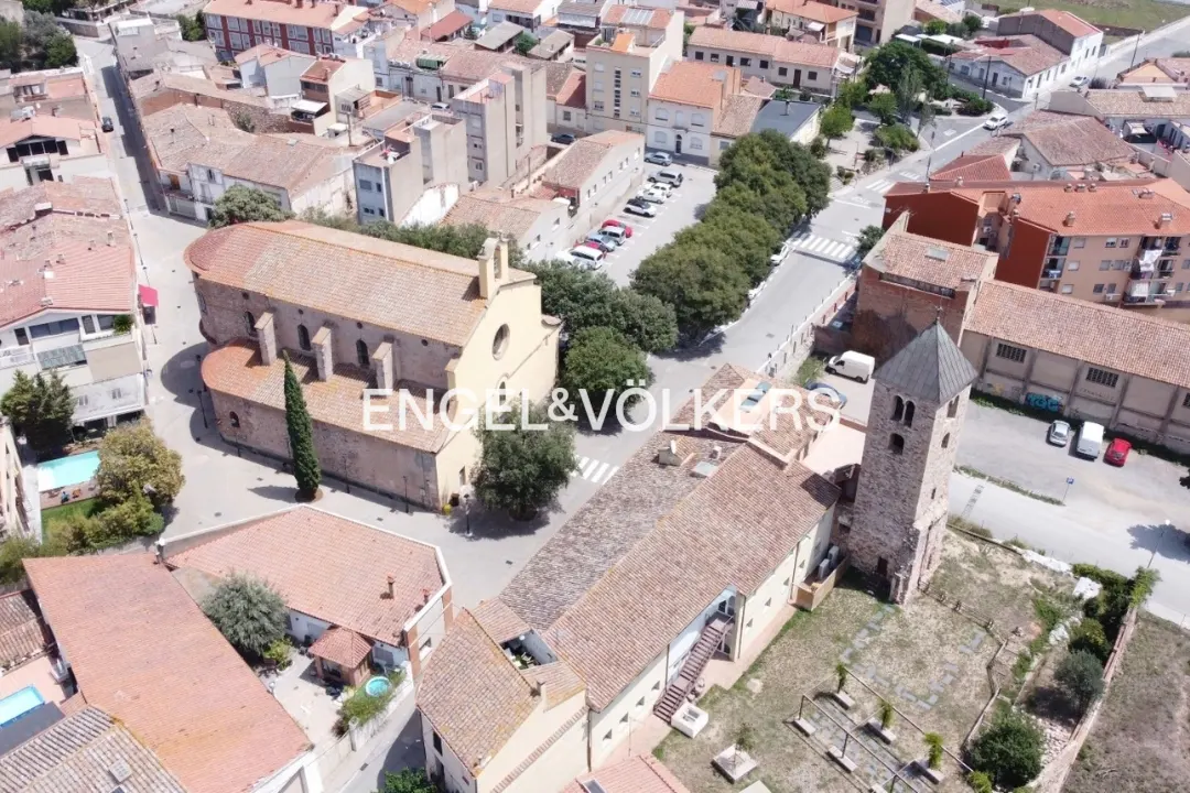 Aerial view of a European town featuring a church with a red tile roof and a tall bell tower. The Engel & Völkers logo is visible.