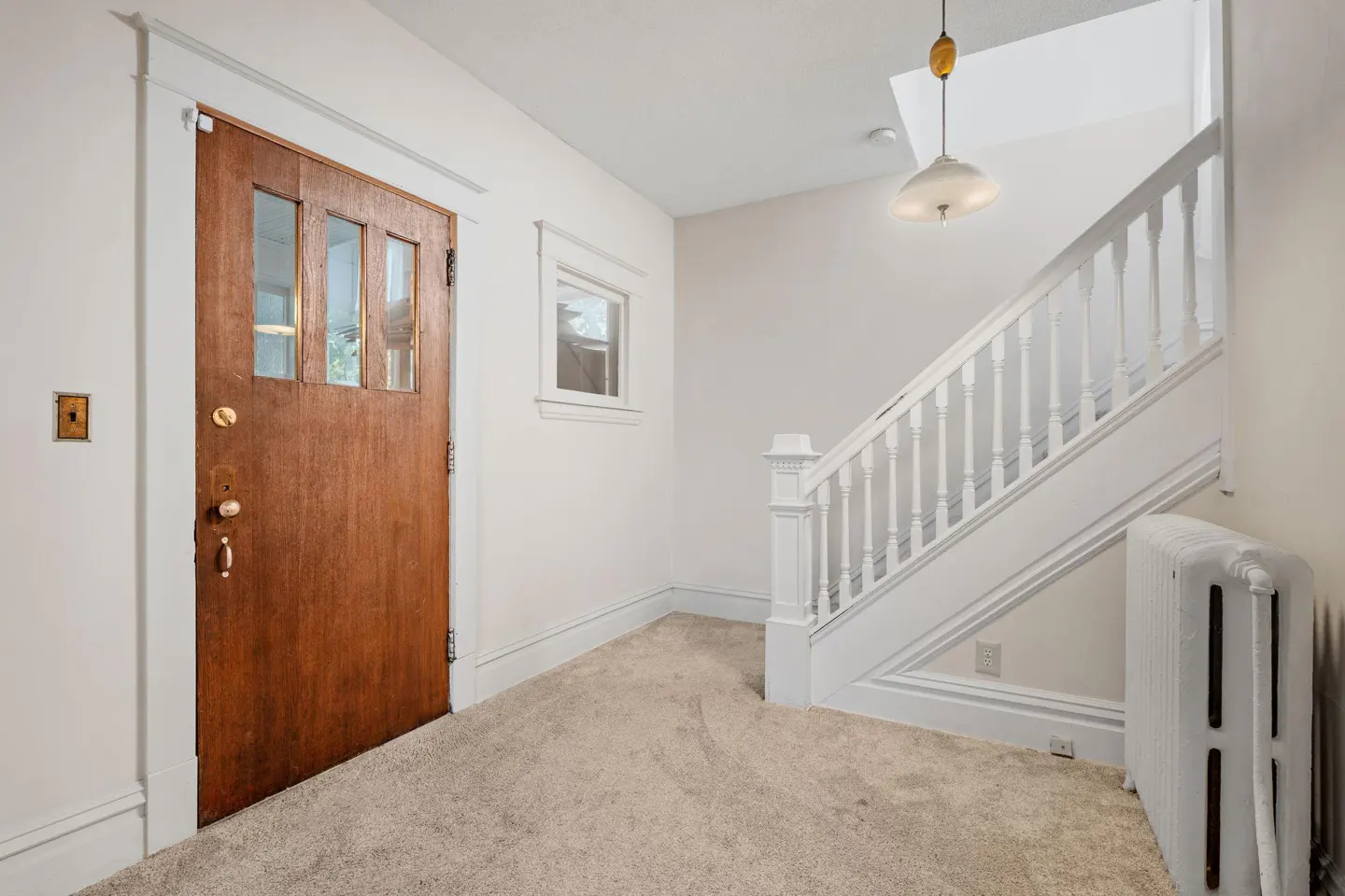 Entryway with a wooden door, white walls, carpeted floor, a white staircase, and a vintage pendant light.