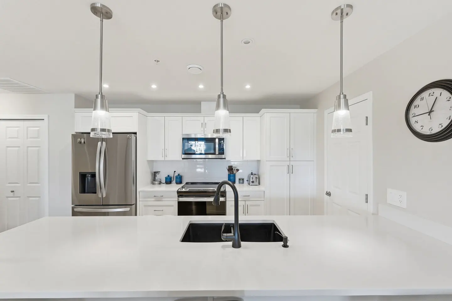 Bright kitchen with white cabinets, stainless steel appliances, and a large white countertop island with a black sink and faucet.