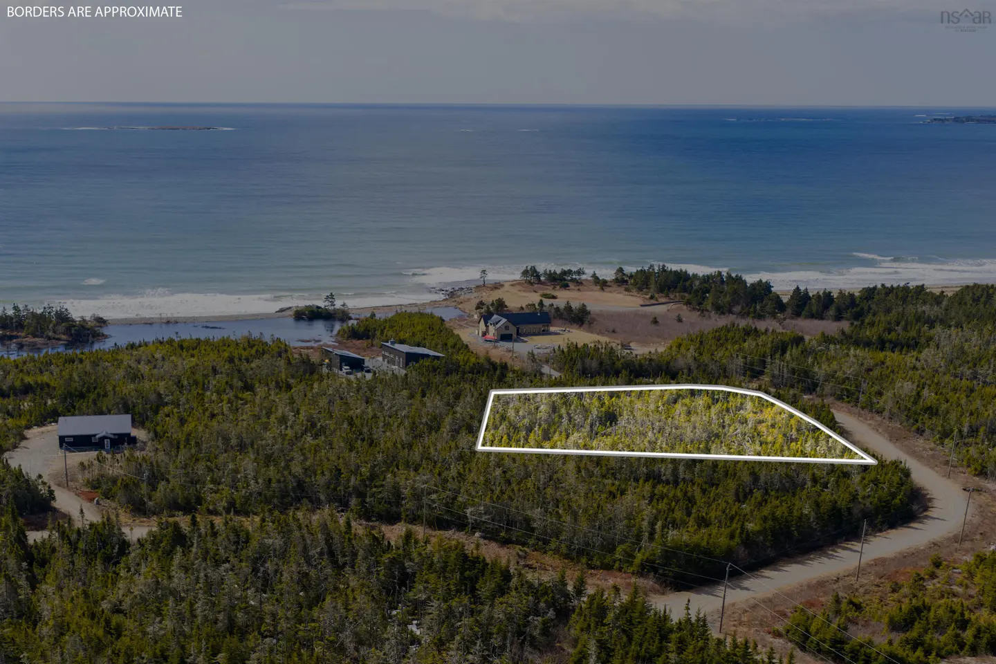 Aerial view of a wooded lot outlined in white, near the ocean and houses.