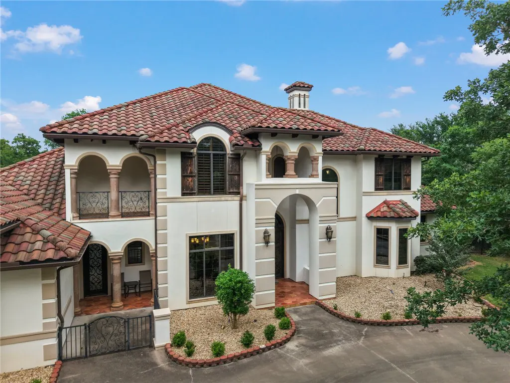 Two-story Mediterranean-style home with a red tile roof, white stucco walls, arched windows, and a circular driveway.