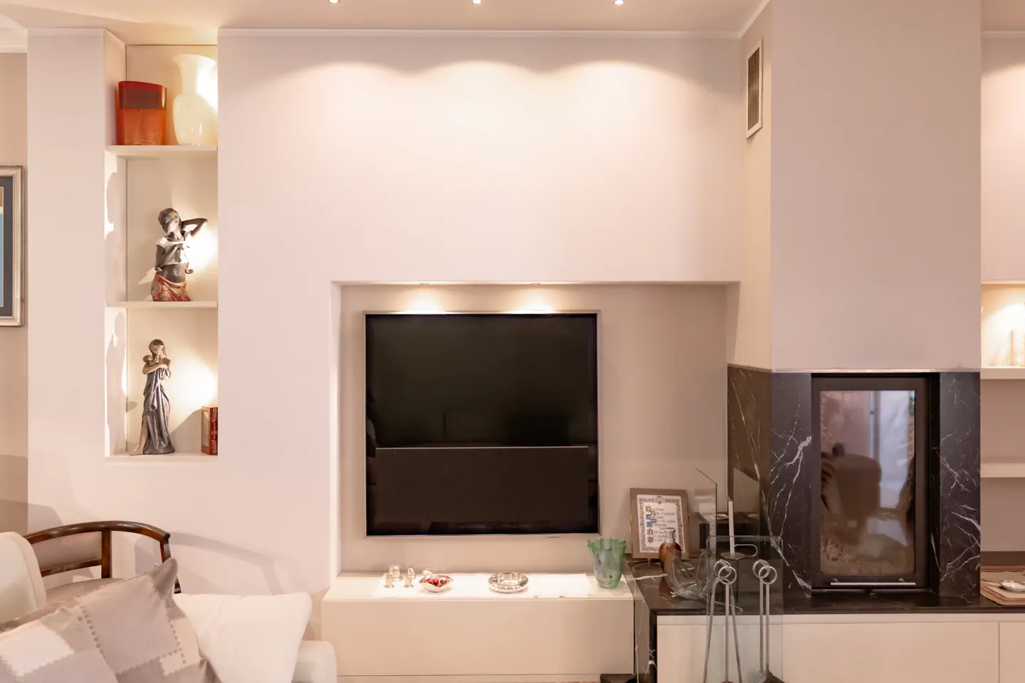 Modern living room wall with a mounted TV, recessed shelving featuring decorative figurines, and a black marble fireplace.