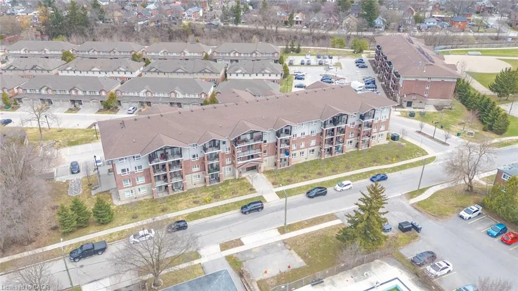 Aerial view of a multi-story apartment building with brown roof and brick facade, surrounded by trees and parked cars.