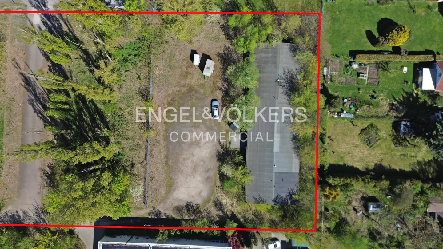 Aerial view of a commercial property outlined in red, featuring a building, parking area, and surrounding greenery.