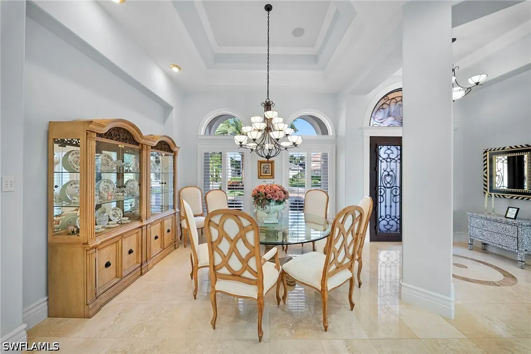 Bright dining room with a glass table, six chairs, and a wooden china cabinet. A chandelier hangs above the table.