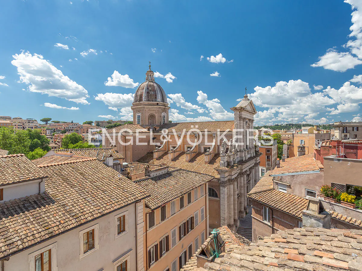 High-angle view of a historic Roman church with a large dome, surrounded by terracotta-roofed buildings under a blue sky.