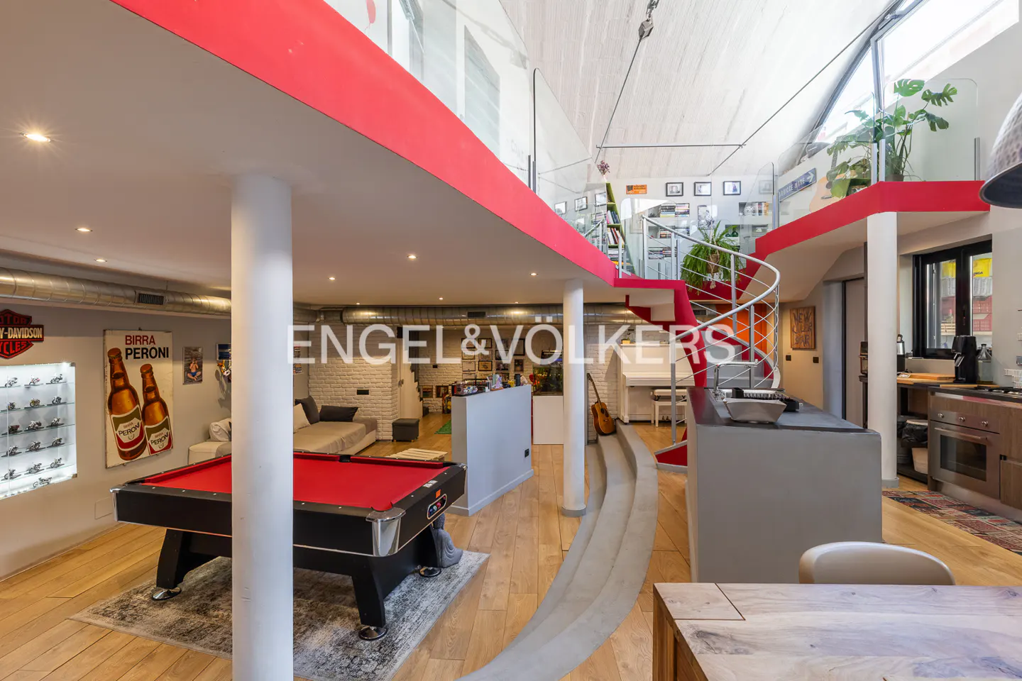 Open-concept loft with a red pool table, spiral staircase, and kitchen. The walls are white and the floors are light wood.